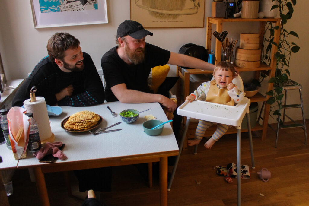 Två män sitter och försöker mata sitt barn.