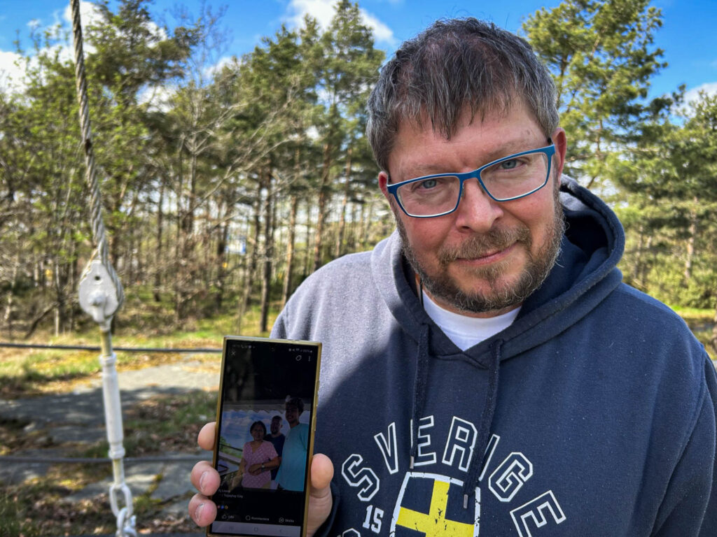 Ted Litens visar upp en bild på sin telefon. På bilden ser man Ted, hans fru och son.