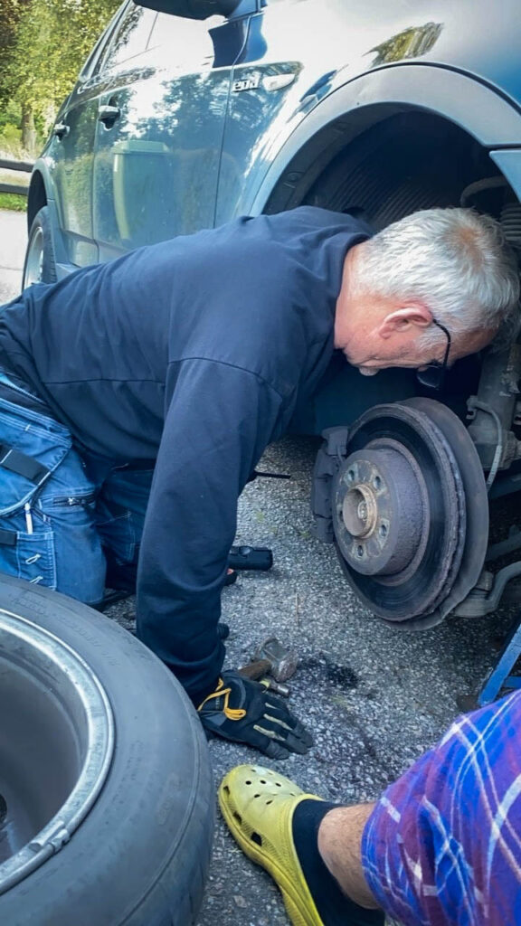 Senad står på alla fyra framför en bil och byter däck. 
