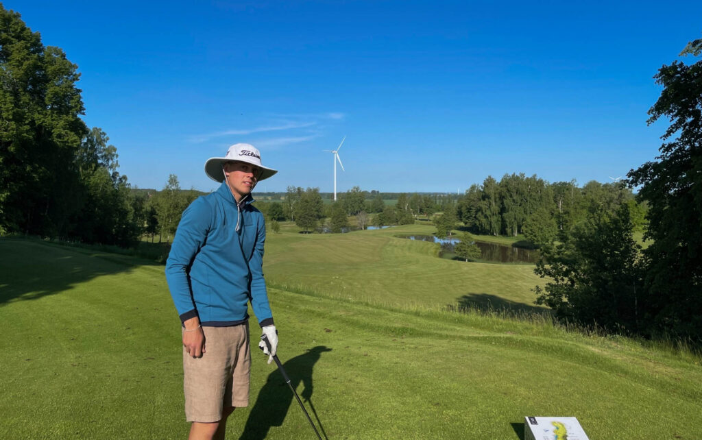 Julius Hallén står på golfbanan. I handen håller han en golfklubba och han har en golfhatt på sig.